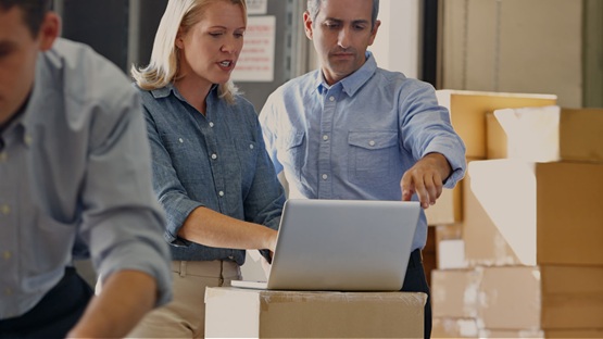Osoby w magazynie korzystają na laptopie z automatyzacji procesów w e-commerce, w tle kartony.