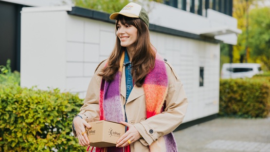 Kobieta stojąca przed maszyną Paczkomat InPost z paczką w dłoni.