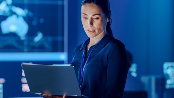 Kobieta zajmująca się e-commerce marketing automation w pomieszczeniu z laptopem, wokół ekrany z wykresami.