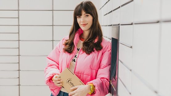 Dziewczyna w różowej kurtce trzyma notes, stojąc przy maszynie Paczkomat.