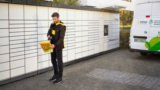 Uśmiechnięty kurier pracujący w InPost dostarcza paczki do maszyny Paczkomat.