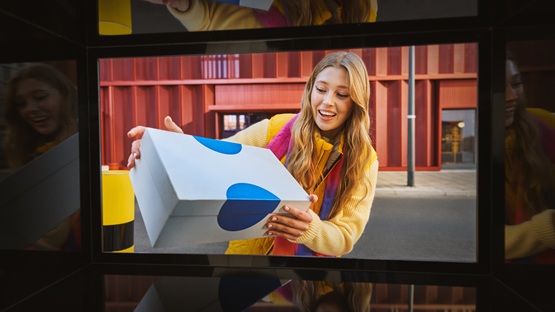 Kobieta z uśmiechem nadaje paczkę przez Paczkomat, co pokazuje, jak łatwo można wysłać paczki, w tym prezenty, korzystając z tej wygodnej usługi.