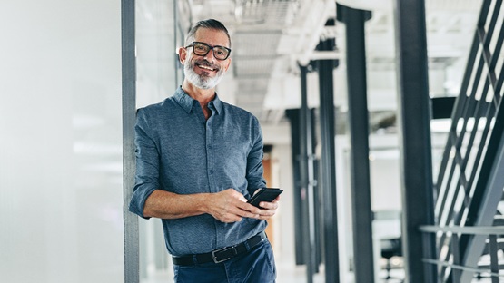 Uśmiechnięty specjalista od machine learning w e-commercew nowoczesnym biurze, trzymający smartfon.