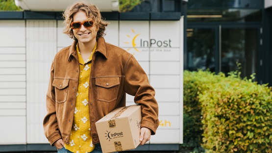 Uśmiechnięty chłopak przed maszyną Paczkomat, trzymający paczkę