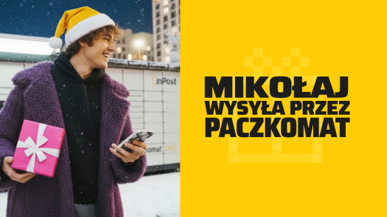 Uśmiechnięty chłopak w czapce Mikołaja stojący pod maszyną Paczkomat z telefonem w ręce.