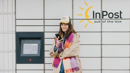 Kobieta stojąca przed maszyną Paczkomat InPost ze smartfonem.