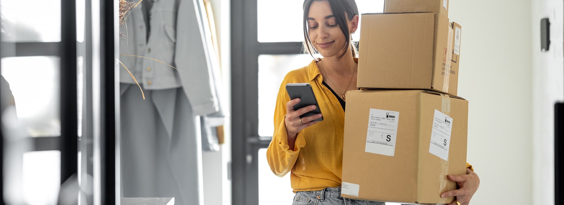 Osoba trzymająca telefon i trzy kartony w pomieszczeniu jednocześnie korzystająca z ułatwień AI w logistyce.