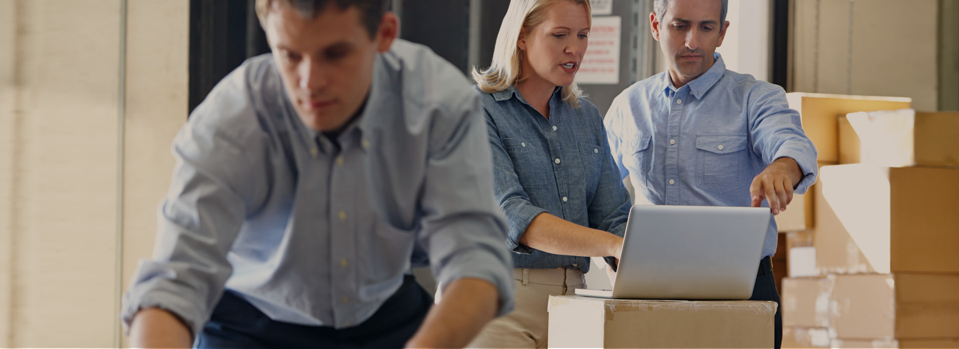 Osoby pracujące przy laptopie w magazynie z kartonami i zajmujące się automatyzacją zamówień.