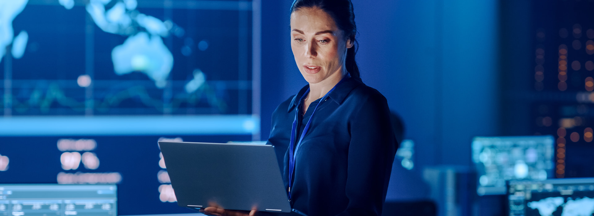 Kobieta zajmująca się e-commerce marketing automation w pomieszczeniu z laptopem, wokół ekrany z wykresami.