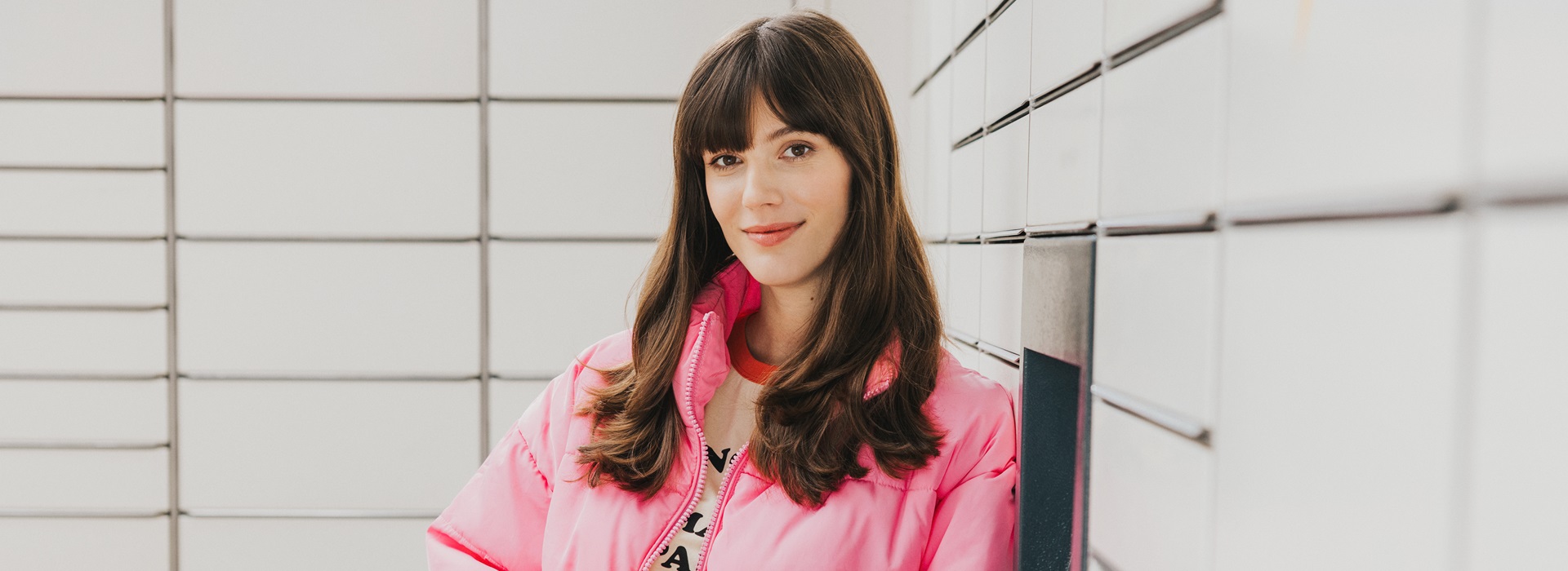 Dziewczyna w różowej kurtce trzyma notes, stojąc przy maszynie Paczkomat.