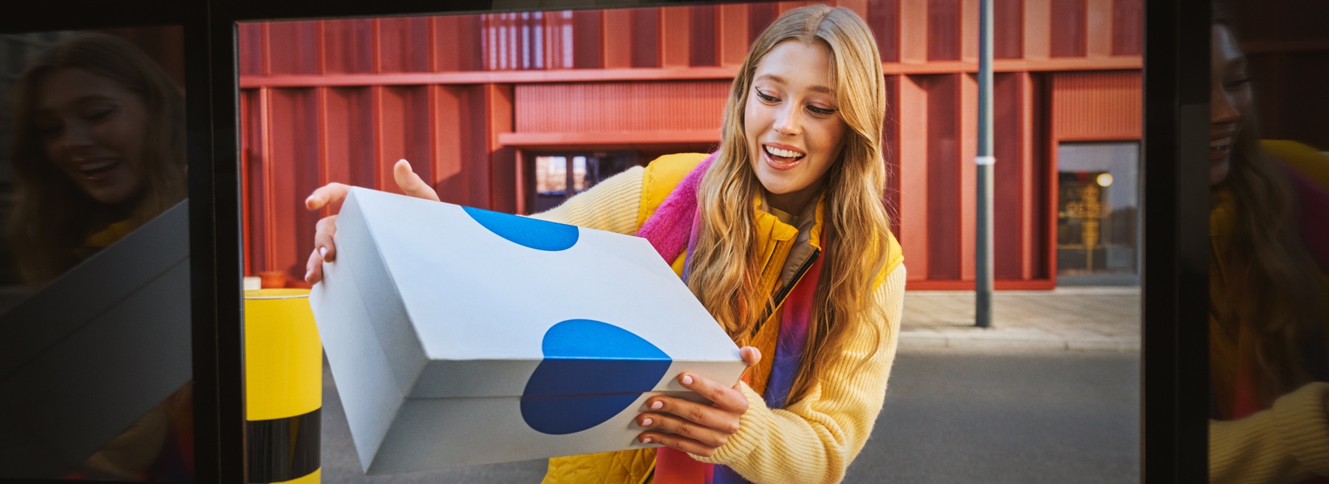 Kobieta z uśmiechem nadaje paczkę przez Paczkomat, co pokazuje, jak łatwo można wysłać paczki, w tym prezenty, korzystając z tej wygodnej usługi.