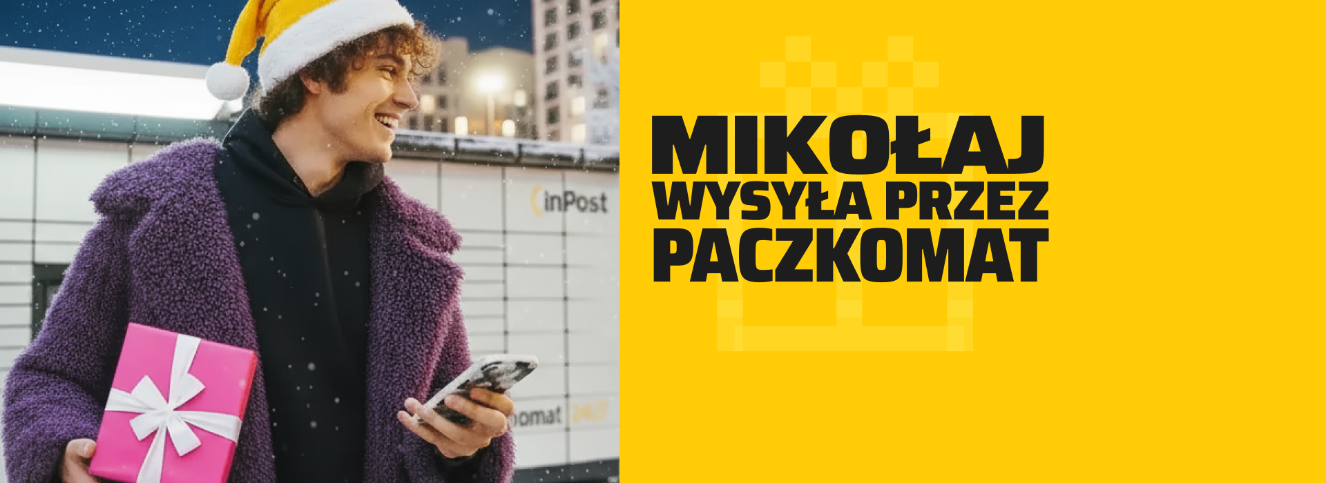 Uśmiechnięty chłopak w czapce Mikołaja stojący pod maszyną Paczkomat z telefonem w ręce.