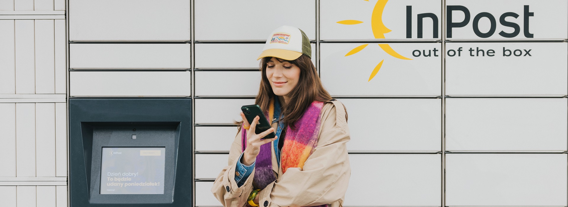 Kobieta stojąca przed maszyną Paczkomat InPost ze smartfonem.