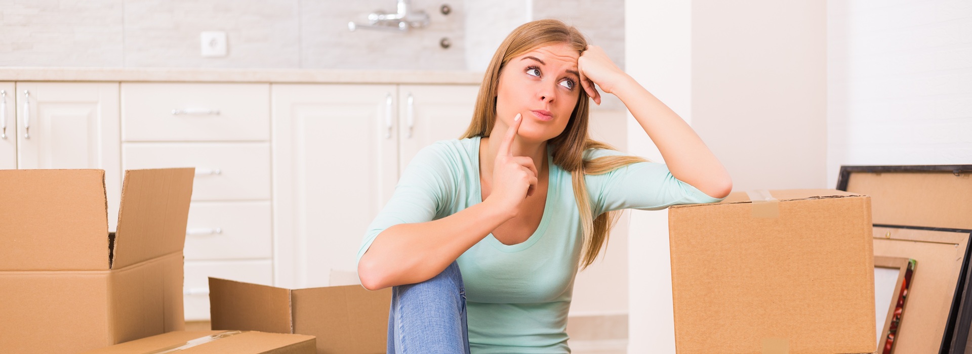 Kobieta pakuje rzeczy do przeprowadzki za granicę. Obok niej kilka kartonów gotowych do wysyłki przez Paczkomat.