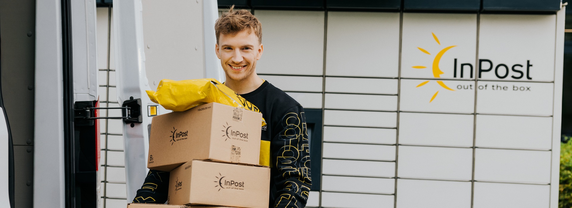 Kurier trzymający trzy paczki przez maszyną Paczkomat InPost.