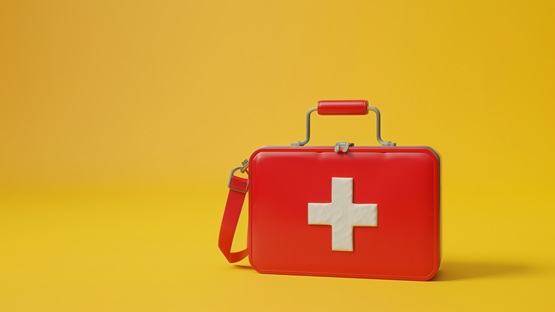 Czerwona apteczka z białym krzyżem na żółtym tle, symbolizująca pierwszą pomoc i gotowość do działania w sytuacjach nagłych.