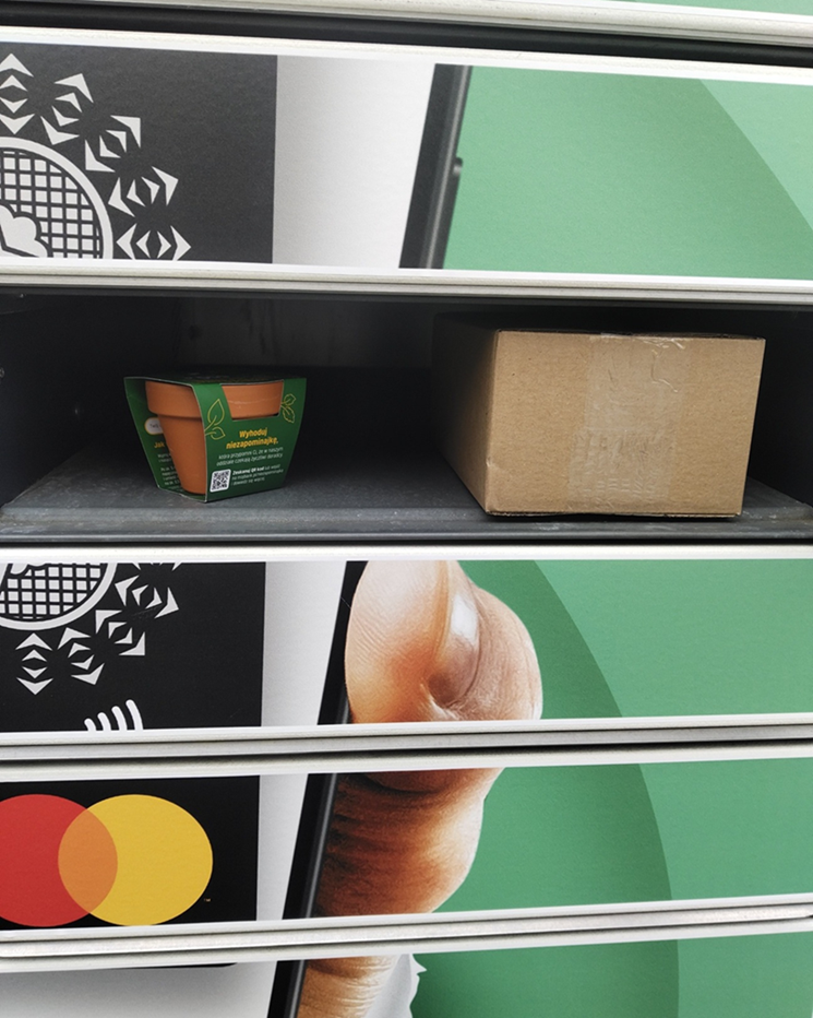 Otwarta skrytka urządzenia Paczkomat w specjalnej okleinie Banków Spółdzielczych z Grupy BPS i Mastercard. W środku niezapominajka oraz paczka.