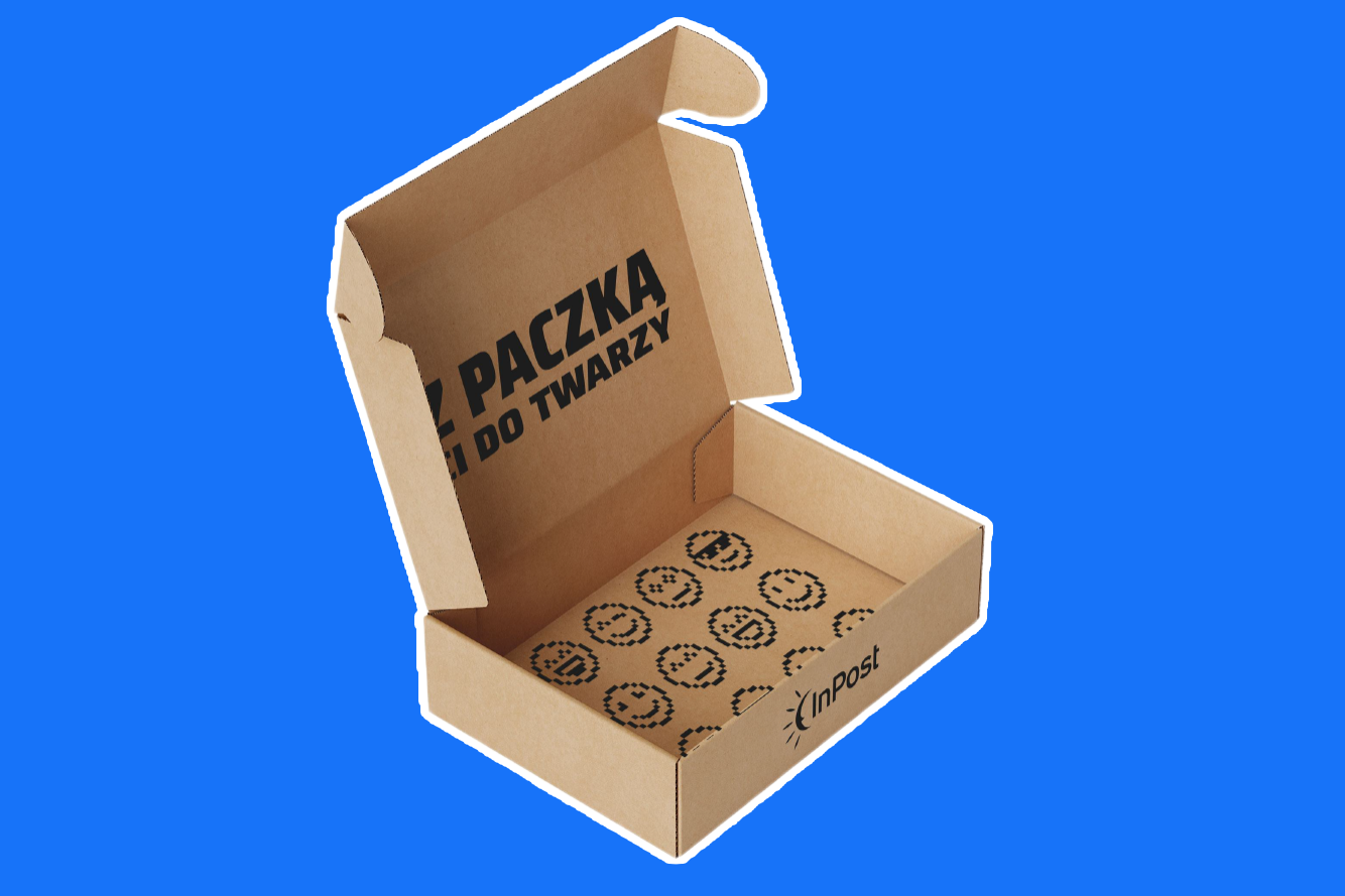 Otwarte kartonowe opakowanie z logo InPost, radosnymi emotikonami nadrukowanymi na dnie i napisem wewnątrz "Z paczką Ci do twarzy".