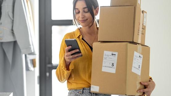 Osoba trzymająca telefon i trzy kartony w pomieszczeniu jednocześnie korzystająca z ułatwień AI w logistyce.