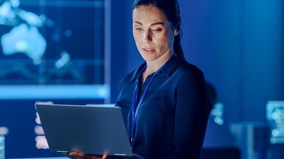 Kobieta zajmująca się e-commerce marketing automation w pomieszczeniu z laptopem, wokół ekrany z wykresami.