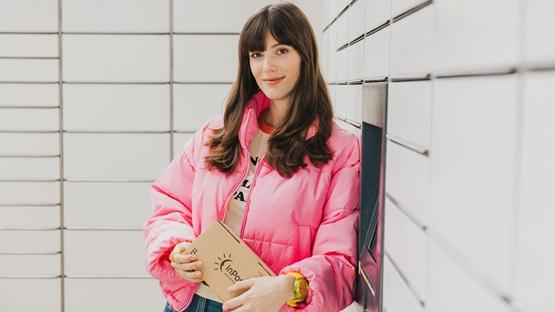 Dziewczyna w różowej kurtce trzyma notes, stojąc przy maszynie Paczkomat.