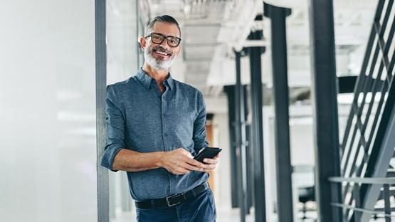 Uśmiechnięty specjalista od machine learning w e-commercew nowoczesnym biurze, trzymający smartfon.