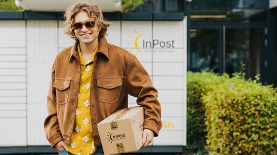Uśmiechnięty chłopak przed maszyną Paczkomat, trzymający paczkę