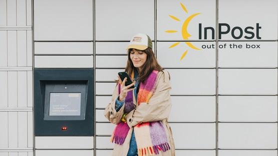 Kobieta stojąca przed maszyną Paczkomat InPost ze smartfonem.