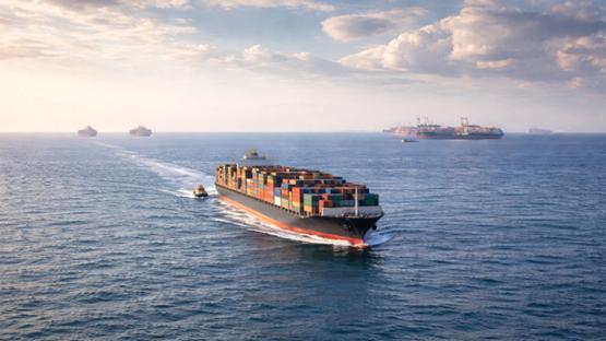 Transport morski frachtowy: z oddali widoczny statek kontenerowy płynący po otwartym morzu, z kolorowymi kontenerami na pokładzie.