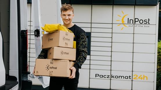 Kurier trzymający trzy paczki przez maszyną Paczkomat InPost.